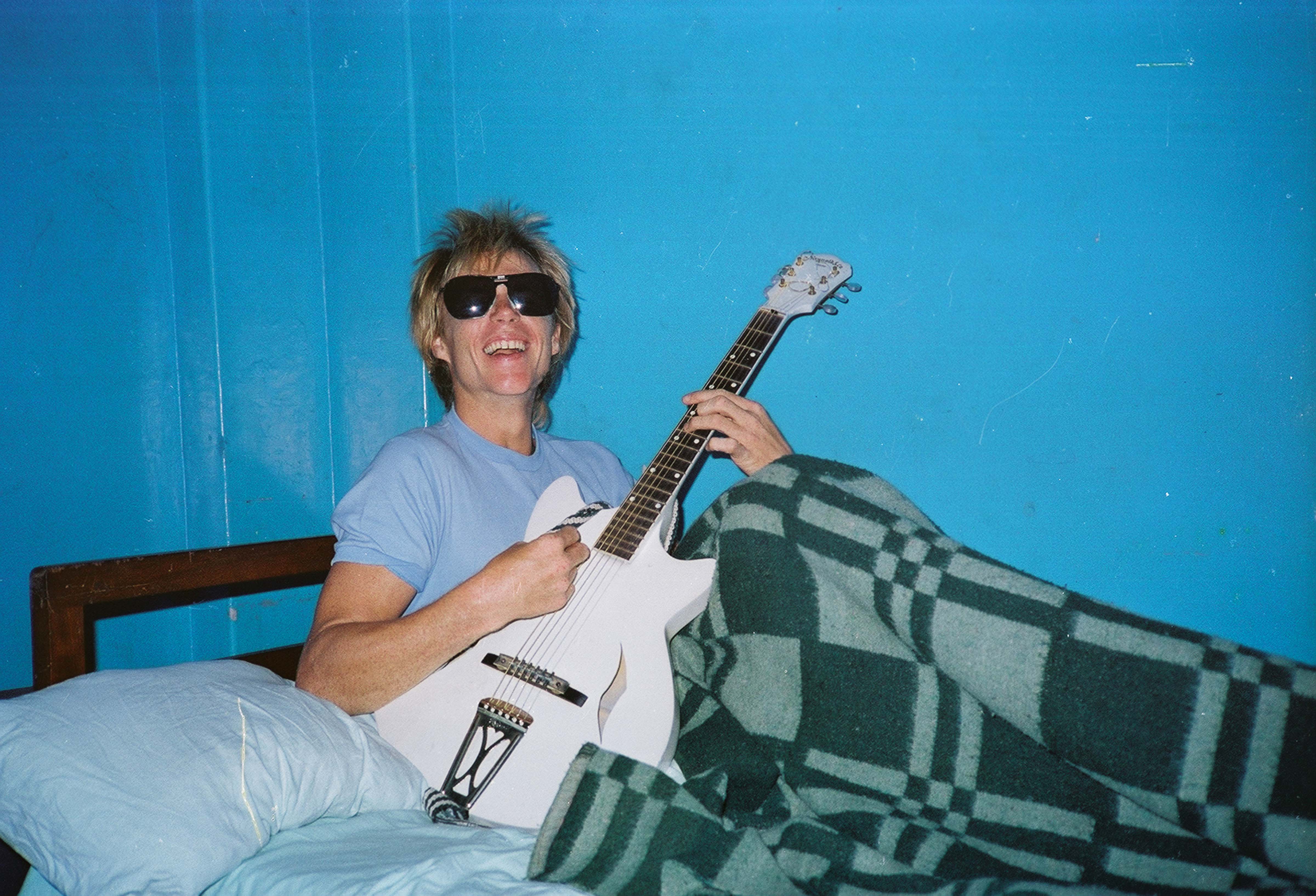 Jeff Shea On Bed With Guitar At Nyandarua Hotel